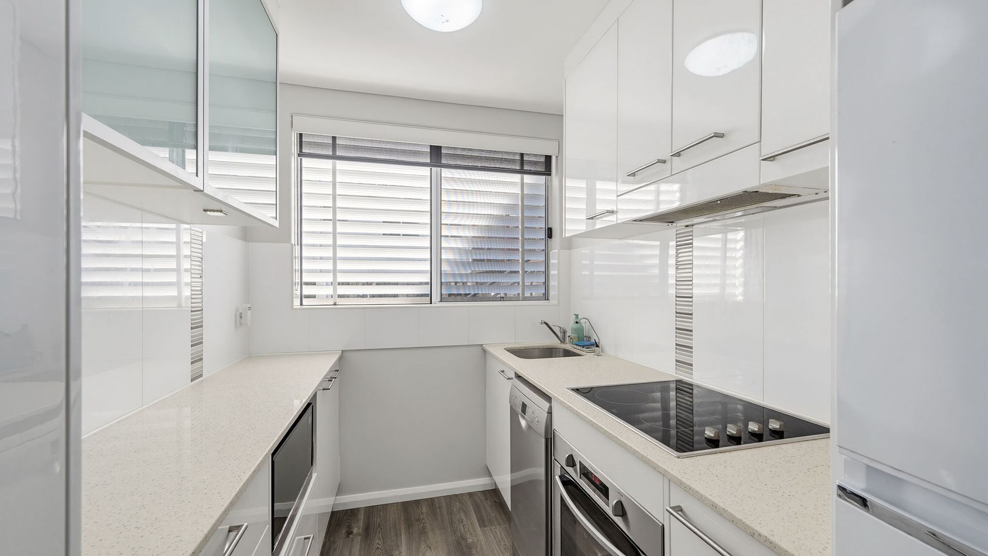 A compact kitchen with white cabinetry, a built-in oven, and a window with blinds.