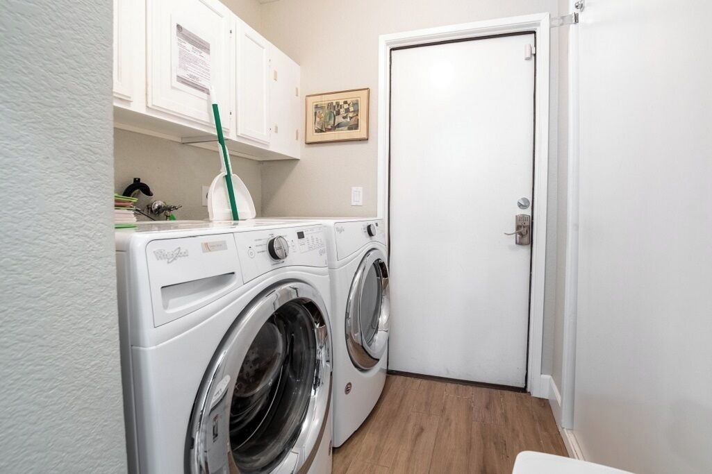 Een kleine wasruimte met een voorlader wasmachine en droger, een klein kastje boven de wasmachine, en een deur aan de rechterkant.