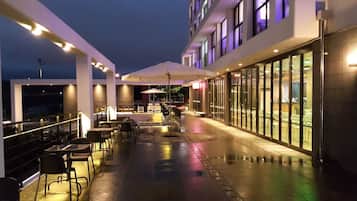 An outdoor patio area with tables and chairs, a covered seating area, and a view of the building's exterior.