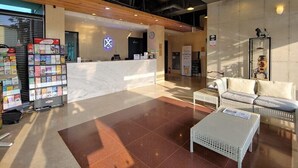 A lobby with a reception desk, seating area, and a display of magazines. - Hotel Stay Interview Jeju (Seogwipo)