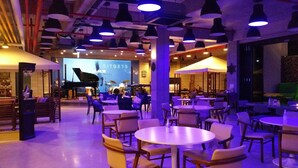 A spacious indoor area with multiple seating arrangements, including round tables and chairs, and a stage with musical instruments. - Hotel Stay Interview Jeju (Seogwipo)