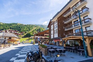 A hotel with outdoor seating, a checkered pavement, and a mountain backdrop. - 100m from ski slopes, 1st floor, balcony, parking, tv, ski locker, 28m², Valloire (Valloire)