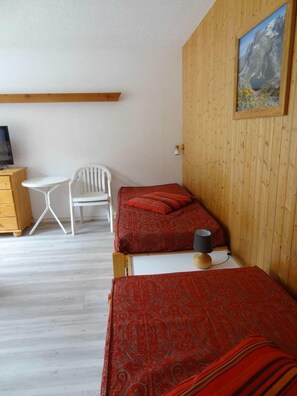 A room with two beds, a desk, a chair, and a painting on the wall. - 100m from ski slopes, 1st floor, balcony, parking, tv, ski locker, 28m², Valloire (Valloire)