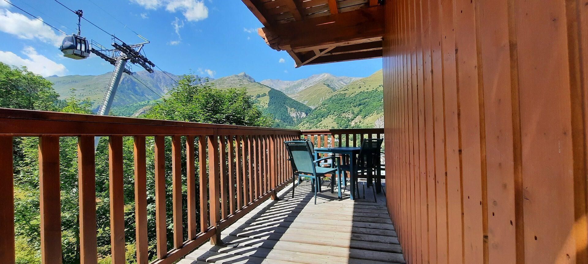A wooden deck with a view of mountains, a cable car, and outdoor seating.