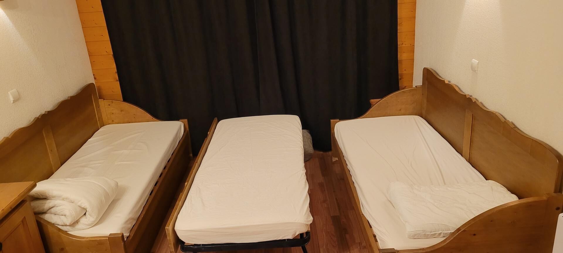 A room with two wooden beds, a black curtain, and a wooden floor.