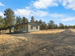A small, single-story house with a gabled roof, a fenced yard, and a gravel driveway. - Ranch Cabin w/ Game Room | Pool, Ping Pong, Arcade (Sisters)