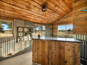 A wooden interior with a bar area, large windows, and a view of the outdoors. - Ranch Cabin w/ Game Room | Pool, Ping Pong, Arcade (Sisters)
