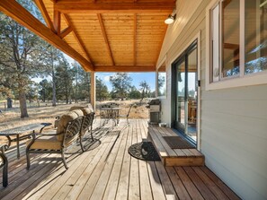 Une terrasse extérieure couverte, dotée d’un plancher en bois, de mobilier en métal et d’un barbecue.