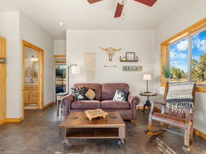 A spacious living room with a leather sofa, a coffee table, and a view of the outdoors. - Ranch Cabin w/ Game Room | Pool, Ping Pong, Arcade (Sisters)