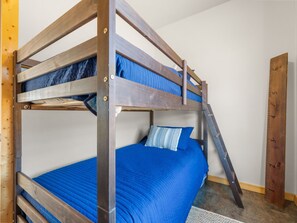 A bunk bed with a ladder, a blue mattress, and a patterned pillow.