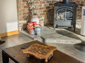 A cozy room with a fireplace, a wooden table, and a basket of board games. - Ranch Cabin w/ Game Room | Pool, Ping Pong, Arcade (Sisters)