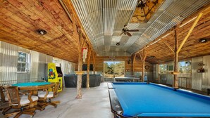 Une table de billard dans un décor intérieur rustique, avec des murs en bois et un sol en béton.