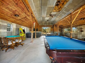 A pool table in a rustic indoor setting with wooden walls and a concrete floor. - Ranch Cabin w/ Game Room | Pool, Ping Pong, Arcade (Sisters)