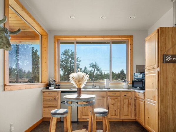 A modern kitchen with wooden cabinets, a large window, and a dining area with stools.