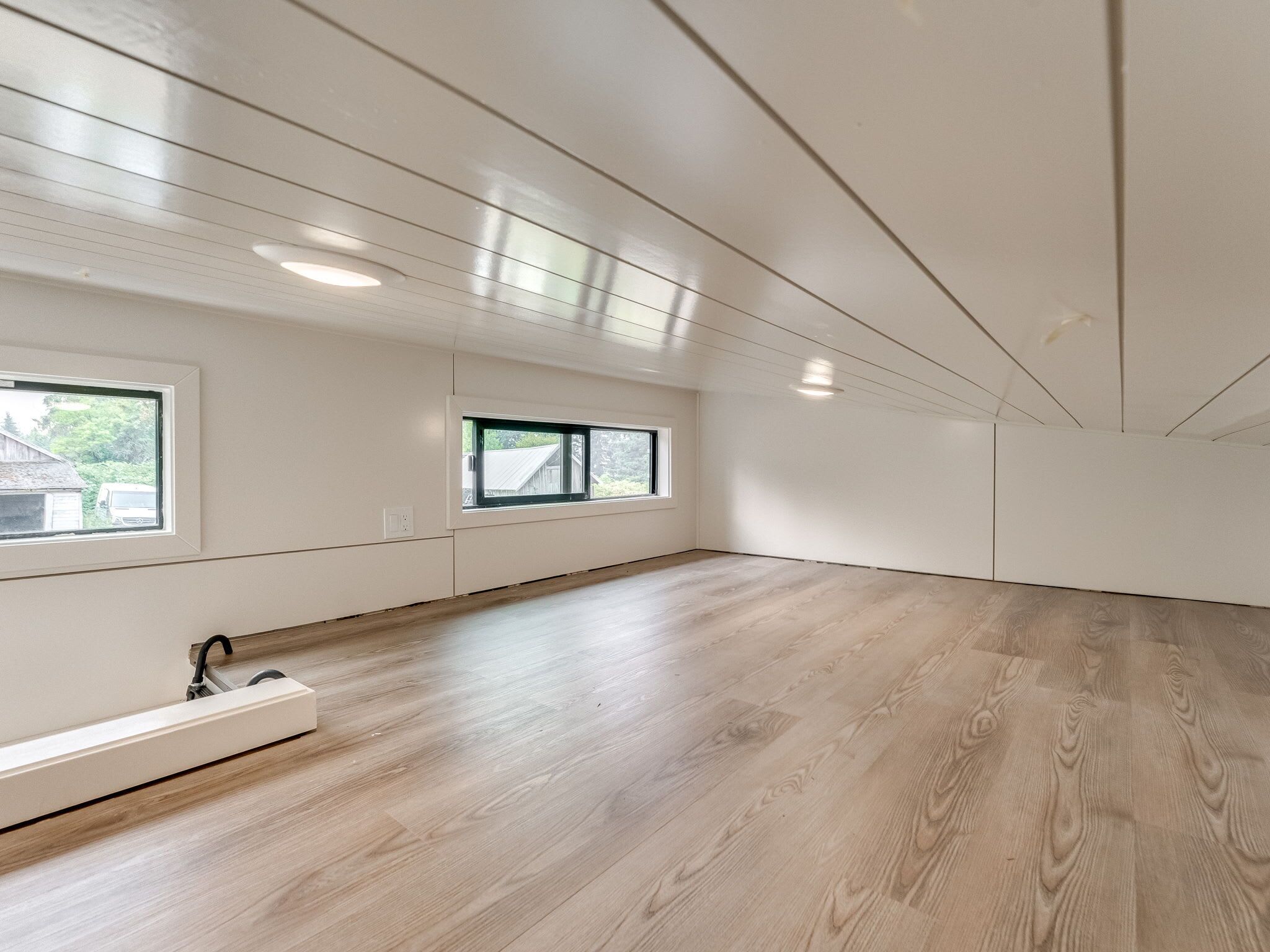 A spacious room with wooden flooring, two windows, and a built-in bench.