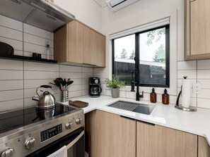 A modern kitchen with a gas stove, a coffee maker, and a window with a view of the outdoors. - Designer Tiny Home Near Lacamas Lake (Camas)