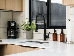 A modern kitchen with a coffee maker, a potted plant, a black faucet, and two brown bottles on the counter. - Designer Tiny Home Near Lacamas Lake (Camas)