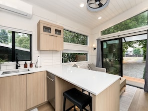 A modern kitchen with a large island, wooden cabinets, and a view of the outdoors. - Designer Tiny Home Near Lacamas Lake (Camas)