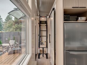 A narrow kitchen with a stainless steel refrigerator, wooden cabinets, and a black metal ladder. - Designer Tiny Home Near Lacamas Lake (Camas)