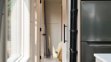 Un pasillo estrecho con una puerta que da a una habitación, un refrigerador a la derecha y una ventana a la izquierda.
