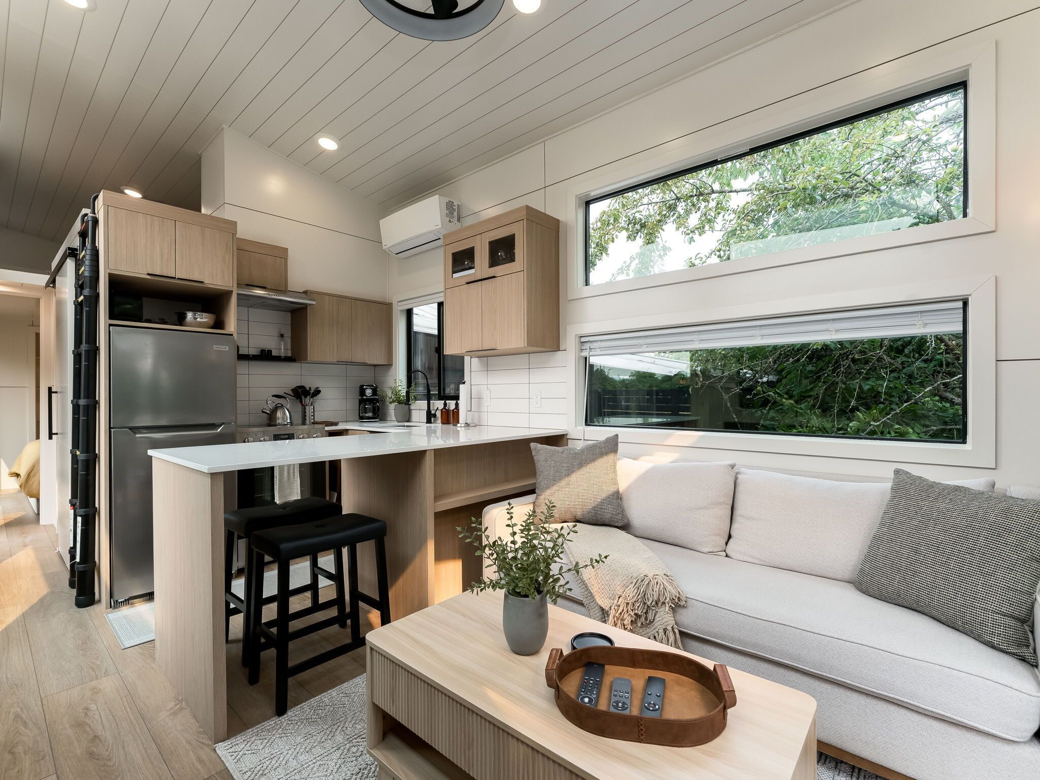 A modern kitchen with a central island, a dining area with a sofa, and a large window providing a view of greenery.