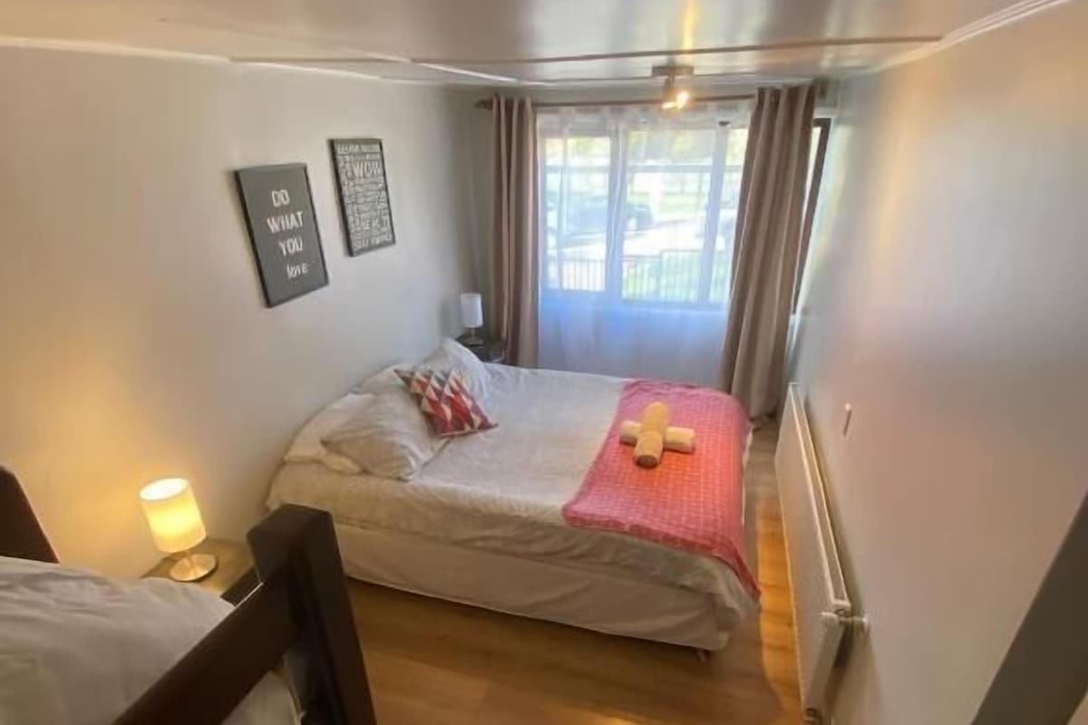 A small, cozy room with two beds, a wooden floor, and a window with curtains.