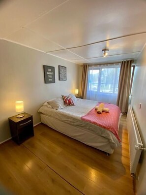 A bedroom with a bed, a nightstand, a window with curtains, and two wall-mounted motivational posters. - Patagon Backpackers (Coyhaique)