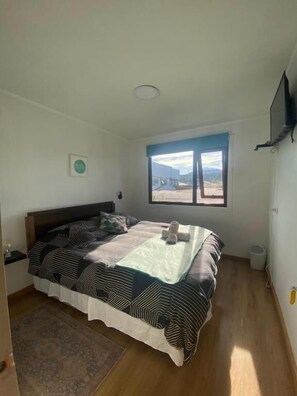 A bedroom with a bed, a window, a television, and a view of the outdoors.