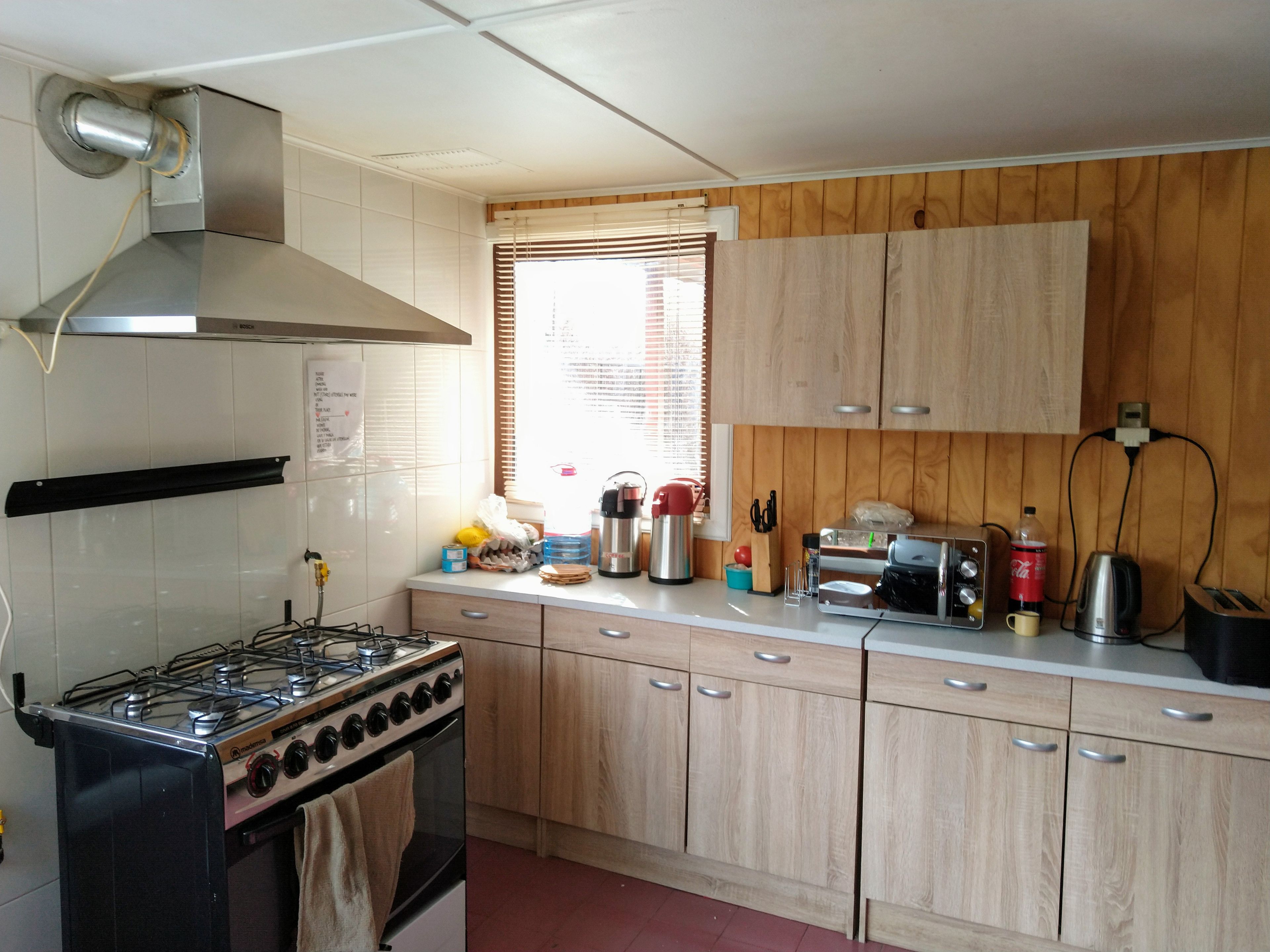 A kitchen with a gas stove, oven, wooden cabinets, and various appliances including a toaster and kettle.