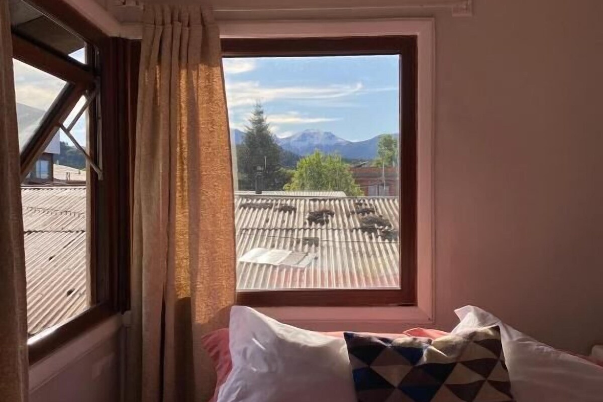 A room with a bed, a window with curtains, and a view of mountains.