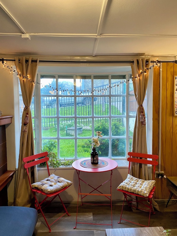 Una habitación con dos sillas rojas, una mesa redonda pequeña con un florero, y vistas a un paisaje verde a través de un ventanal grande.