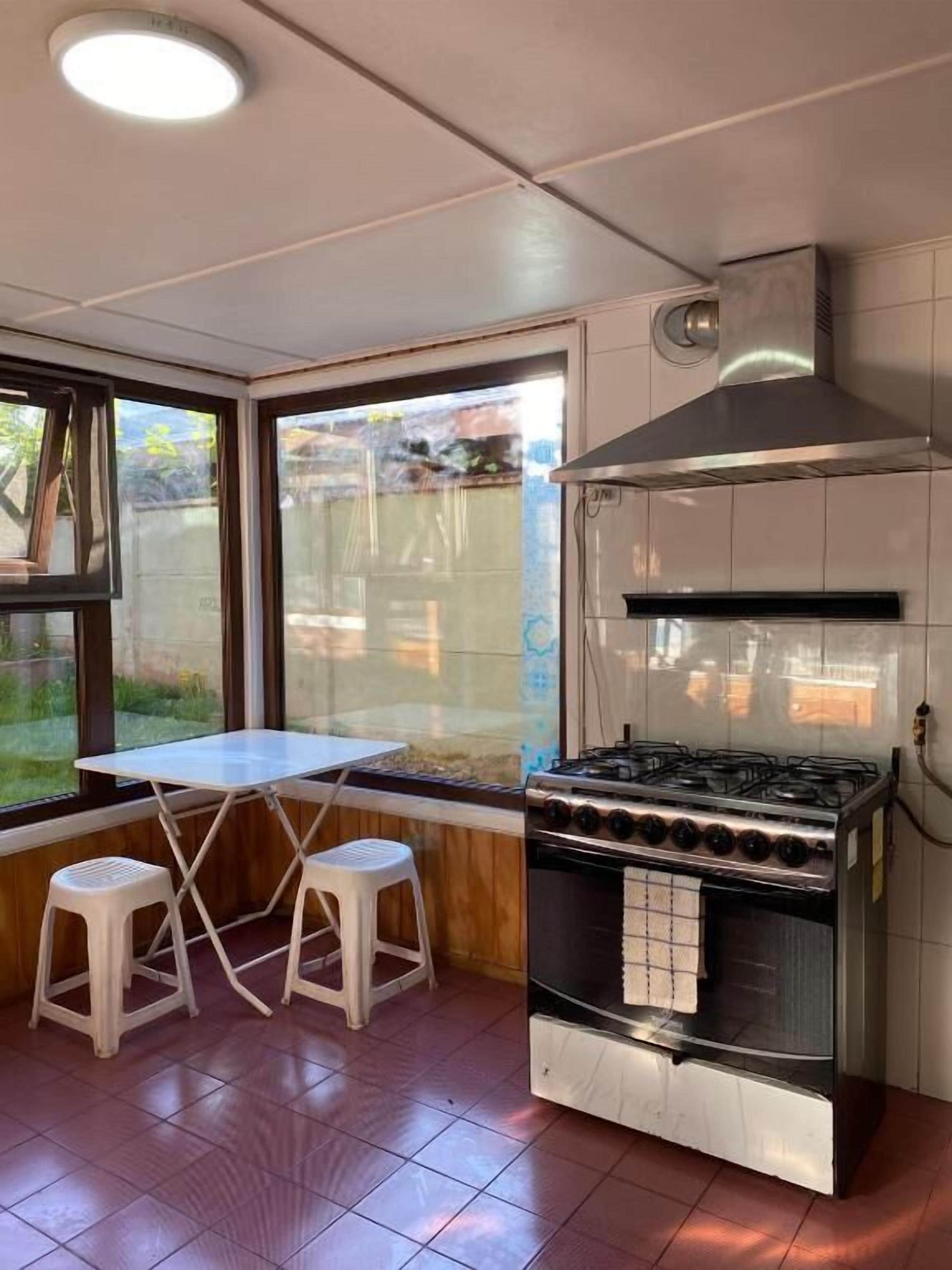 Una cocina con estufa a gas, campana extractora y ventana con vistas al exterior.