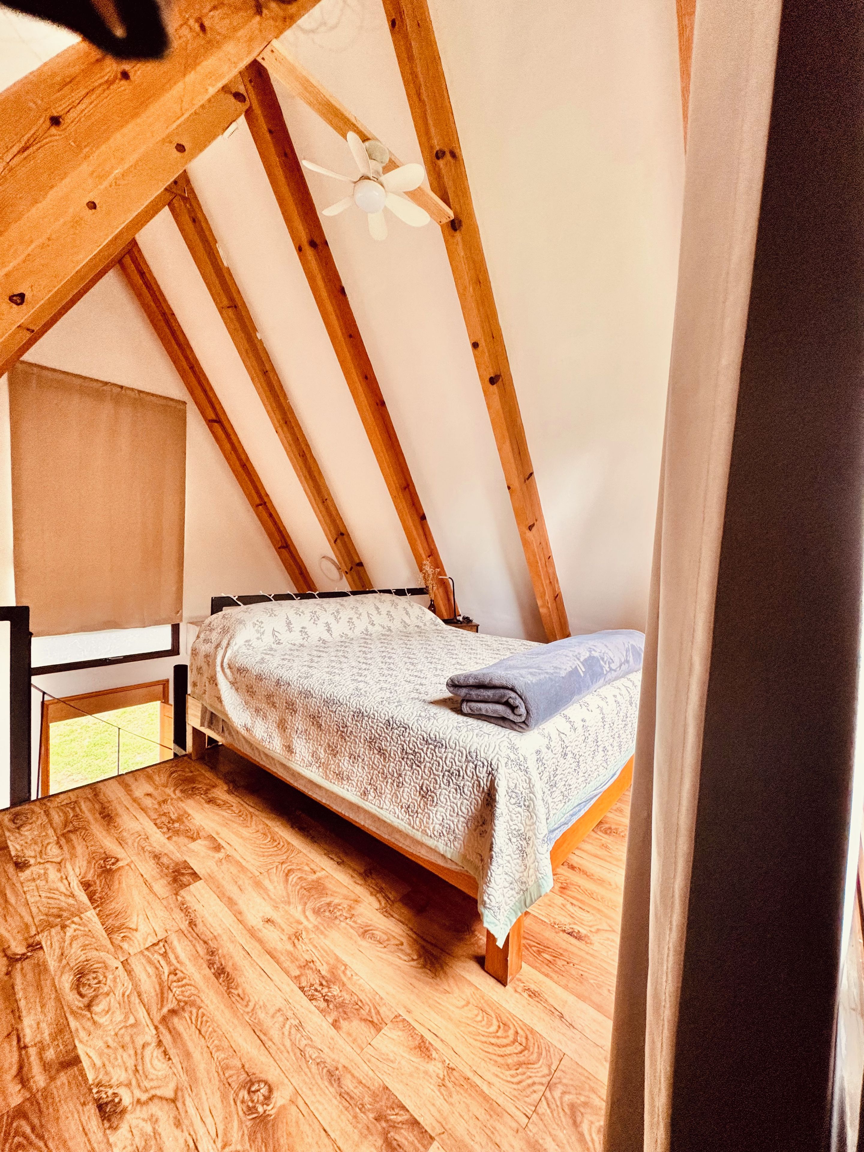 Une petite chambre avec un lit simple, un plafond en pente et des poutres en bois.