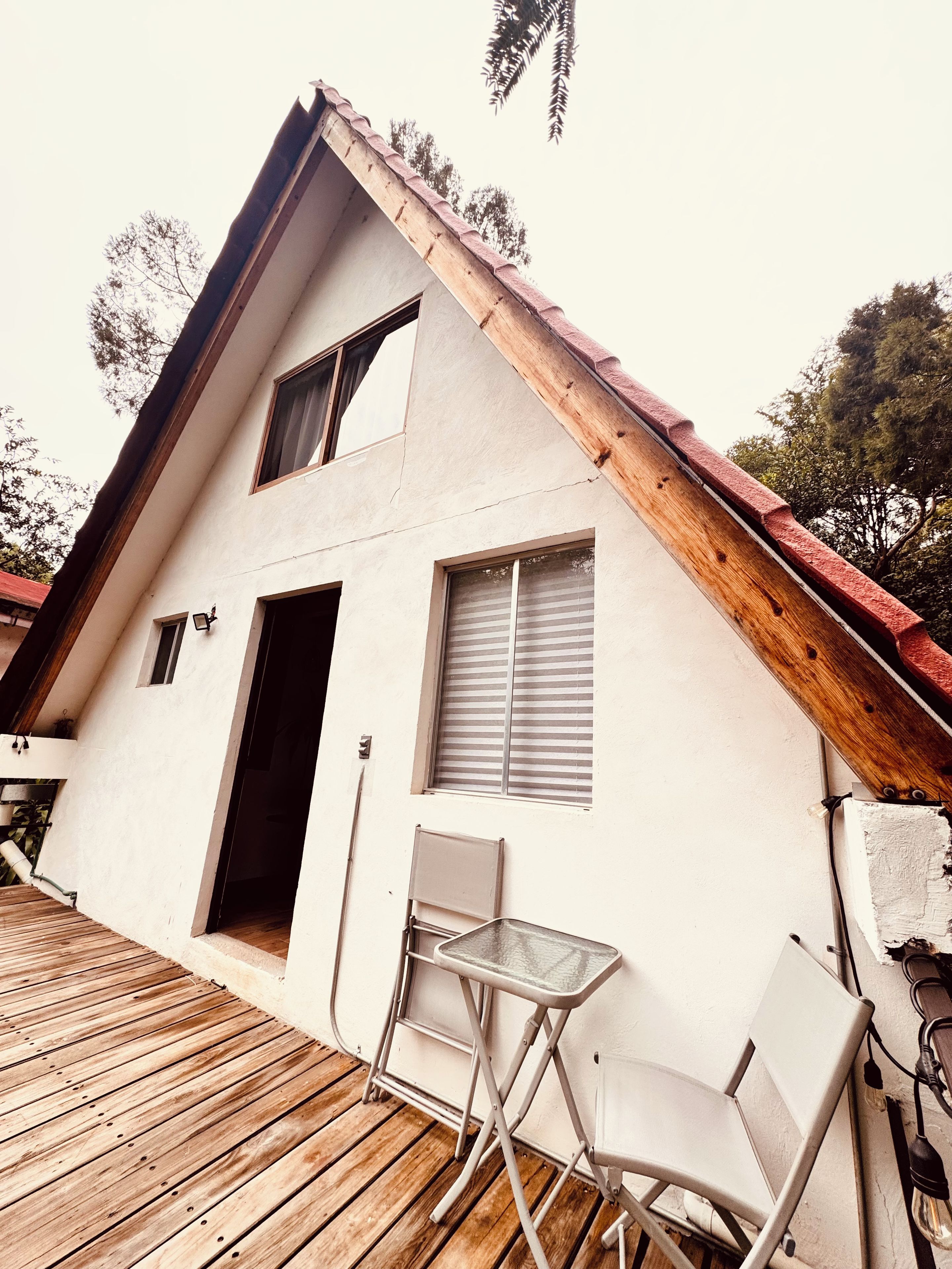 Un bâtiment à deux étages, doté d’un toit en pente, d’une terrasse en bois et d’un petit espace extérieur aménagé avec une table et des chaises.