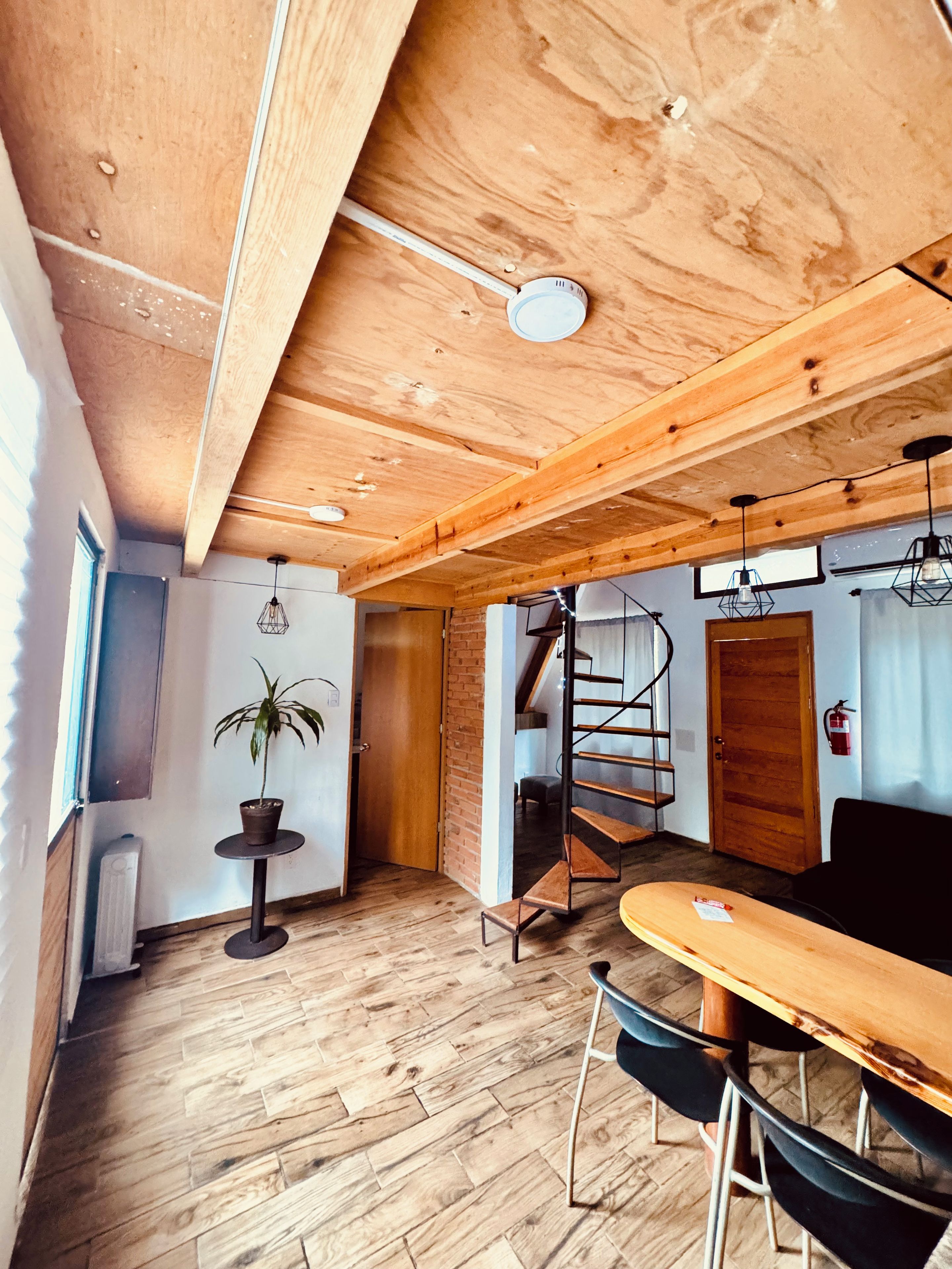 Un intérieur en bois comprenant un coin repas, une plante en pot, un escalier et un extincteur.