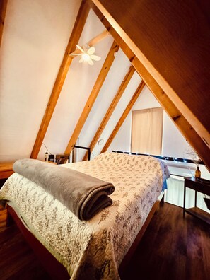 A bedroom with a bed, wooden beams, a ceiling fan, and a window with curtains.