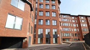 A multi-story brick building with a central entrance, large windows, and a parking area. - Luxury Apartment|Gym, Cinema, work hub & Game Room (London)