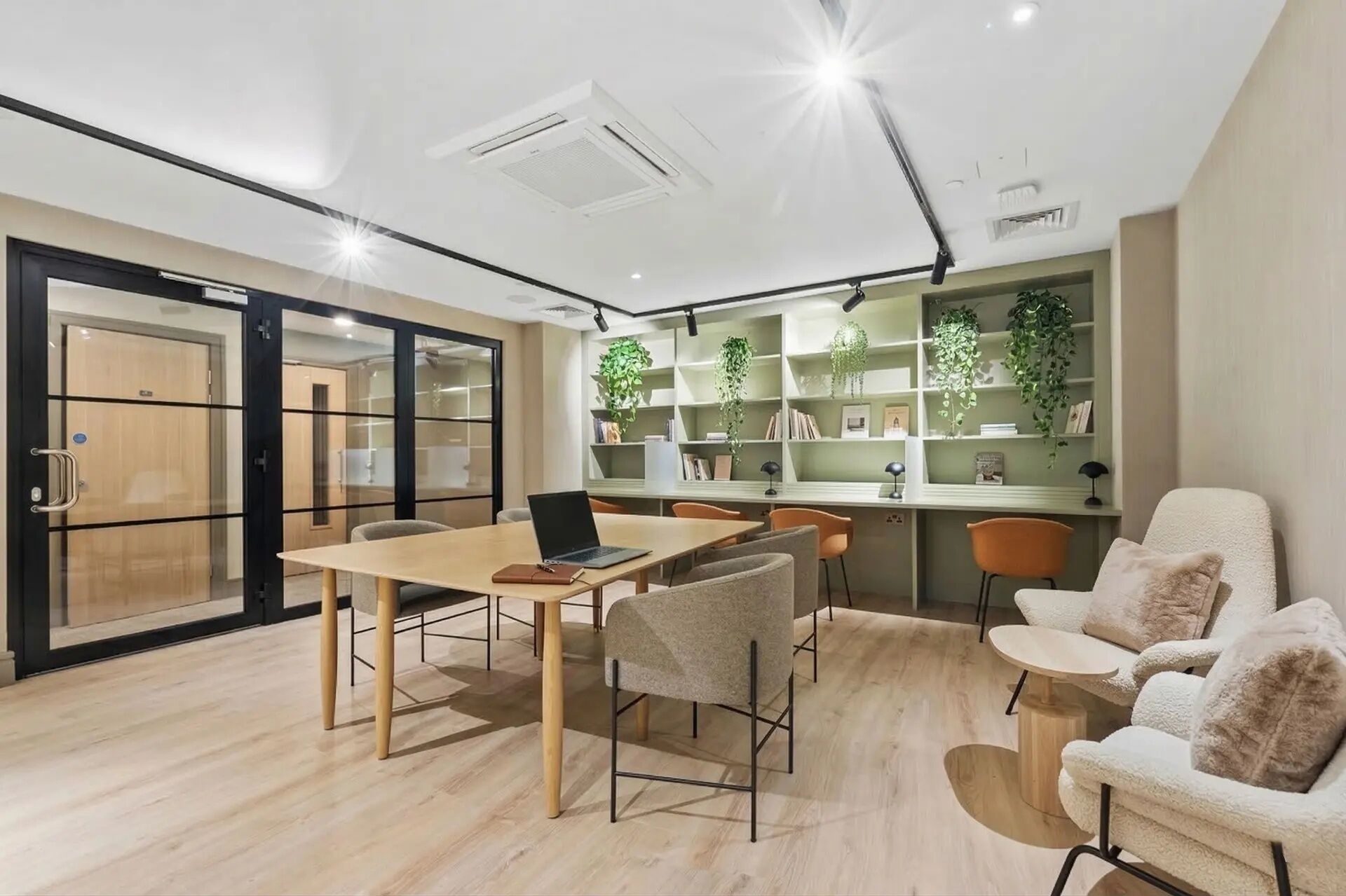 Un espacio de oficina moderno con una mesa de madera, sillas, una computadora portátil y una estantería con plantas.