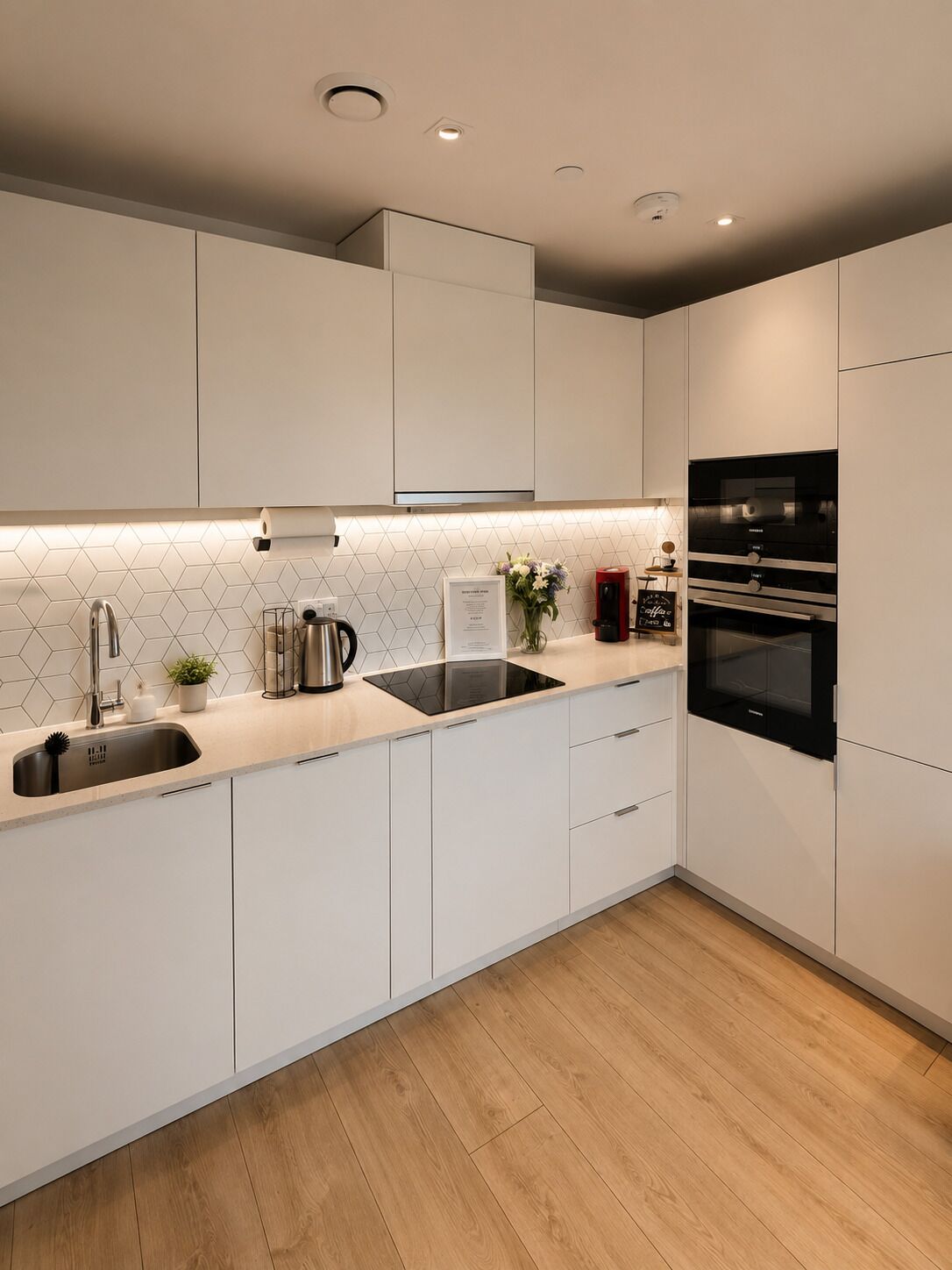 A modern kitchen with white cabinets, a black oven, and a wooden floor.