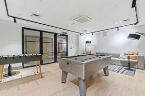 Una mesa de billar en una habitación bien iluminada, con un sofá y una lámpara.