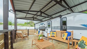 A covered outdoor deck with wooden furniture and a white RV with 'CRUISE LITE' branding. - Private Camper (Rio Grande)