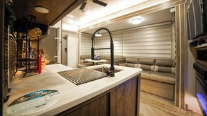 A compact kitchen with a modern sink, a ceiling fan, and a seating area with a sofa. - Private Camper (Rio Grande)