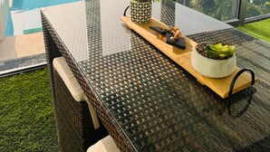 A glass-top table with a wicker chair, a potted plant, and a tray with a bowl of green leaves. - Private Camper (Rio Grande)