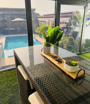 A glass-top table with a wicker chair, a potted plant, and a tray with a bowl of green leaves. - Private Camper (Rio Grande)