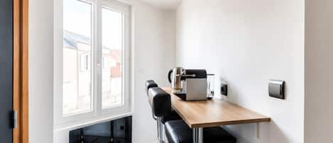 Uma cozinha compacta com janela, uma cafeteira e dois banquetas.