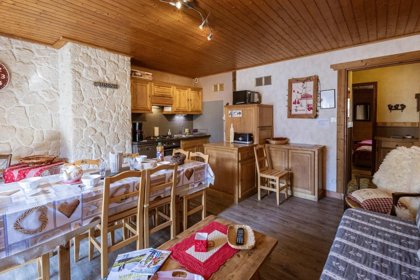 A cozy room with a dining table set for four, wooden cabinets, a kitchen area with a microwave, and a stone wall.