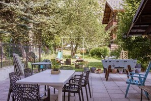 An outdoor patio with a table and chairs, surrounded by greenery and a swing set. - 300m from ski lifts, 3rd floor, balcony, parking, tv, ski locker, 35m², Valloire (Valloire)