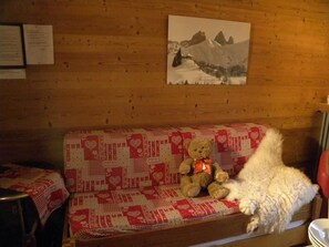 A wooden cabin interior with a sofa covered in a red and white patterned blanket, a teddy bear, and a framed picture on the wall. - 300m from ski lifts, 3rd floor, balcony, parking, tv, ski locker, 35m², Valloire (Valloire)