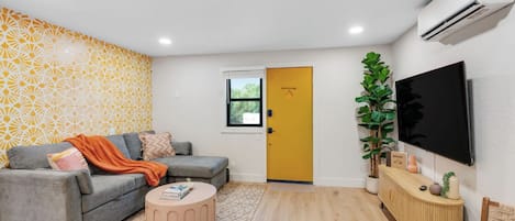 A modern living room with a grey sofa, a round coffee table, and a yellow door.