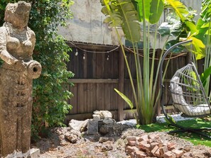 A garden with a stone statue, a wooden fence, a hanging chair, and banana plants. - Modern Design District Home 3 King Beds Near Wynwood (Miami)